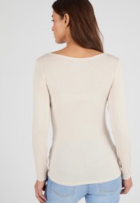 Lichtbeige langelijnige top met een wijde halslijn, aangesloten ontwerp en zachte textuur, gecombineerd met blauwe denim jeans.