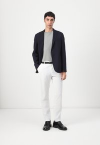 Tengerészkék blézer szürke pólóval, fehér nadrággal és fekete lóferekkel párosítva. Simára csiszolt textúrák; szabott fazon; egyszerű mintázat nélküli design.