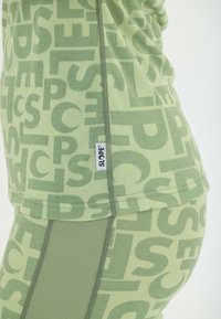 Groene sportkleding met een opvallend letterpatroon, korte mouwen en een aansluitend ontwerp. Inclusief een klein logo-label.