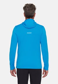 Niebieska bluza z długim rękawem i kapturem, wykonana z lekkiego materiału. Charakteryzuje się dopasowanym krojem oraz logo umieszczonym na górnej części pleców.