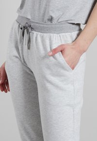 Pantaloni jogger grigi chiari realizzati in un tessuto morbido e testurizzato. Presentano un elastico in vita con cordino e tasche laterali.