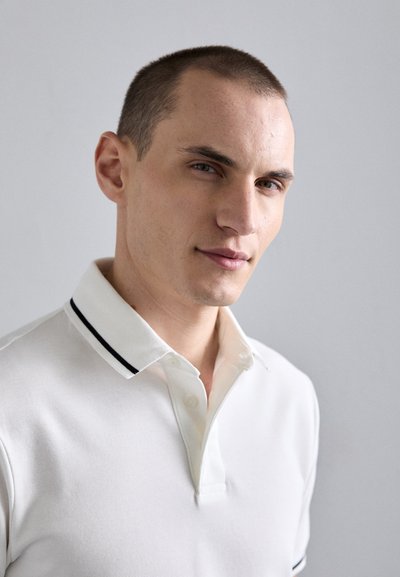Polo shirt in white cotton with a textured pattern, featuring a two-button placket and a black-striped collar detail.