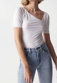 Body bianco a costine con design a spalla sola, maniche corte e silhouette aderente, abbinato a jeans azzurri a vita alta.