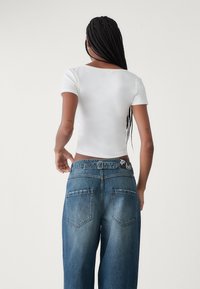 Vitt kortärmat cropped linne med bred halsringning, kombinerat med ljusblå vida jeans som har bakfickor och en kontrasterande midja.