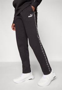 Schwarze Sweatpants aus Baumwolle mit weißem Puma-Logo. Ausgestattet mit seitlichen Streifen mit wiederholtem Logo, gerippten Knöcheln und Seitentaschen.