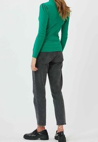 Grön långärmad topp med puffärmar, kombinerad med högmidjade mörkgrå jeans och svarta platåskor, som visar upp färgglada mönstrade strumpor.