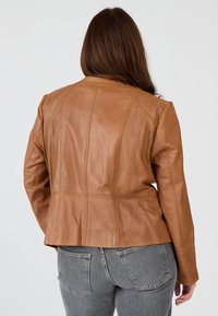 Braune Lederjacke mit einer taillierten Passform, strukturierten Nähten und langen Ärmeln. Kombiniert mit grauen Denim-Jeans, die Rückendetails zeigen.
