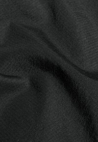 Ingrandimento di un tessuto nero con una sottile texture diagonale e morbide pieghe che creano ombre e luci delicate.