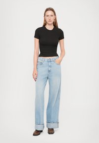 Black fitted short-sleeve top paired with light blue wide-leg jeans, featuring a rolled cuff, lightly distressed texture, and subtle stitching.