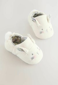 Zapatillas de tela blanca con forma de caras de conejito, que cuentan con detalles bordados y un forro floral colorido, con orejas y un pompón en la parte superior.