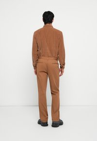 Brown corduroy shirt paired with brown trousers, featuring a tailored fit and minimalistic design. Black footwear completes the outfit.