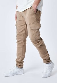 Pantaloni cargo beige con multiple tasche laterali, design slim fit, vita elasticizzata e dettagli di cucitura discreti. Completati da sneakers bianche.