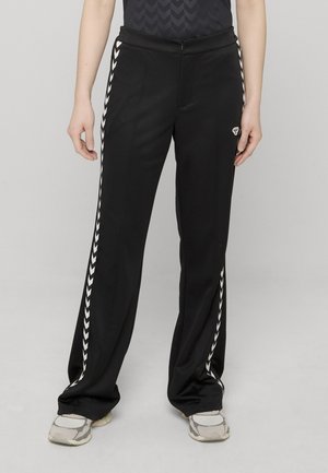 Sorte træningsbukser med afslappet pasform, med hvide chevronstriber langs siden og et lille logo, lavet af glat, let materiale.