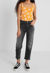 Top de tirantes de flores naranjas con escote cuadrado, combinado con jeans negros desgastados y zapatillas negras con detalles en blanco.