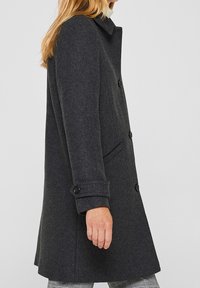 Abrigo de lana gris oscuro con cuello camisero, cierre de botones, bolsillos laterales y mangas con puños. Textura suave con un corte entallado.