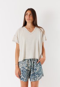 T-shirt beige chiaro a V con maniche corte abbinato a pantaloni corti blu a fantasia con un design a foglie. Il tessuto sembra morbido e traspirante.