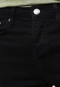 Jeans de denim negro con una textura suave, diseño de cinco bolsillos, cierre de botón metálico y sutiles detalles de costura.