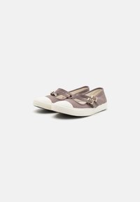 Chaussures slip-on flexibles en tissu taupe doux avec deux sangles croisées et des boucles en ton doré, présentant un embout et une semelle en caoutchouc blanc.