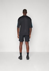 Black athletic shirt with short sleeves, featuring blue accents. Paired with black shorts and black shoes, viewed from the back.