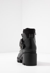 Stivaletti neri sopra la caviglia con tacco spesso, realizzati in pelle e materiale elasticizzato, chiusura laterale con zip e elementi decorativi in metallo.