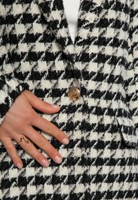 Blazer de patrón de pata de gallo en blanco y negro, hecho de tejido texturizado, con un acento de botón dorado y un corte ajustado.