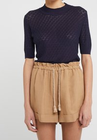 Top corto de punto navy de manga corta con patrón de diamantes; combinado con pantalones cortos beige con cordón y dobladillo vuelto, adornados con borlas.