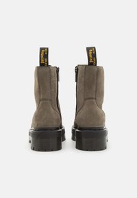 Botines de ante gris con suela de goma negra gruesa, cremallera lateral y tiradores con texto amarillo sobre fondo negro.