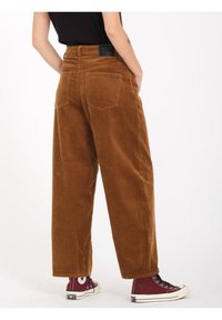 Brune corduroy bukser med brede ben og lodrette ribber, bagpå lomme og et sort mærke i taljen. Sammen med maroon høje sneakers.