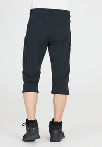 Mustat polvipituiset shortsit, joissa on sileä pinta, kahdella vetoketjullisella takataskulla ja litteällä vyötärönsuunnittelulla. Yhdistetty mustiin vaelluskenkiin.