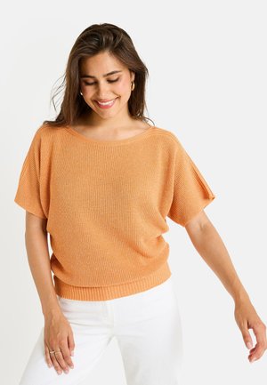 Haut en tricot texturé orange avec une coupe ample, un col large et des manches courtes, associé à un pantalon blanc. Design simple et décontracté.