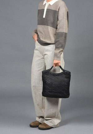 Zwarte geweven handtas met een textuurpatroon, korte handvatten, gedragen bij lichtgrijze wijde broek en een beige gestreepte trui.