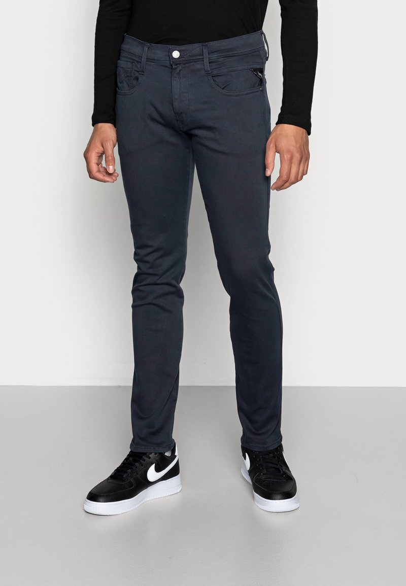 Jeans de corte slim en gris oscuro, fabricados con una suave mezcla de algodón, que cuentan con un bolsillo con cremallera, diseño de cinco bolsillos y una pierna ajustada que se estrecha hacia el tobillo.