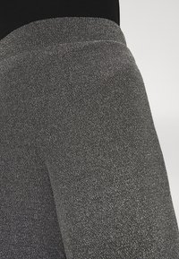 Czarne legginsy z wysokim stanem o metalicznym połysku, wykonane z teksturowanej tkaniny, z gładkim pasem, który zapewnia dopasowaną sylwetkę.