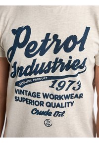 Camiseta de algodón color beige claro con texto en azul oscuro: "Petrol Industries", "1973" y "Vintage Workwear", con un detalle de logotipo circular debajo.