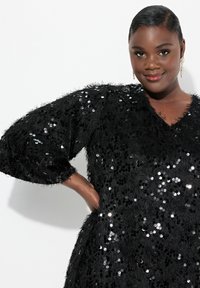 Schwarzes Kleid mit flauschiger Textur, bedeckt mit Pailletten; verfügt über breite Ärmel und einen V-Ausschnitt. Glänzende und strukturierte Details überall.