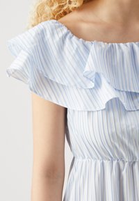 Jasnoniebieska sukienka w białe paski z falbaną na dekolcie bez ramiączek, dopasowana w talii i z lekko opadającą spódnicą. Gładki, lekki materiał.