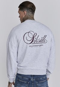 Grauer Sweatshirt mit Rundhalsausschnitt, gerippten Bündchen und dem "Siksilk" Logo in dunkelweinrot auf dem Rücken, mit einer weichen Textur.