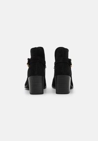Schwarze Wildleder-Ankle Boots mit einem gestapelten Absatz, seitlichem Schnallenverschluss und durchbrochenen Details. Glatte Textur mit runder Zehenform.