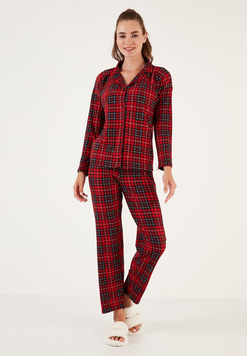 Conjunto de pijama de cuadros rojos con camisa abotonada, mangas largas y pantalones a juego. Tejido suave, corte relajado, detallado con acentos en azul y negro.