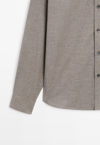 Light brown button-up shirt with long sleeves, a regular collar, and smooth texture, featuring a subtle herringbone pattern and gray buttons.