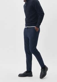 Granatowy sweter z zamkiem przy szyi i granatowe chinosy, w połączeniu z czarnymi mokasynami. Chinosy mają dopasowany krój i boczne kieszenie, wykonane z gładkiego materiału.