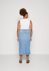 Jeanskjørt i lys blå; midt på leggene med to baklommer; brukt med en hvit ermeløs topp og svarte sandaler.