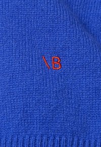 Blå stickad tyg med ett strukturerat mönster, med en liten orange broderad logotyp i det nedre hörnet.