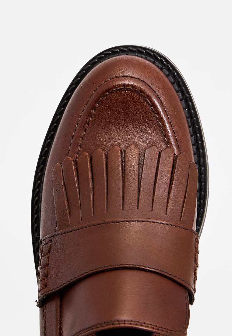 Zapato de cuero marrón con un diseño plisado en la puntera, forma redondeada y suela de goma negra. Textura suave con detalles de costura visibles.