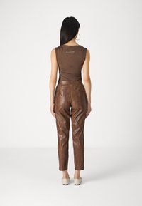 Bruine mouwloze top met gedrapeerd detail; hooggekraagde bruin slangenprint broek; crème instappers; grote oorbellen; gladde textuur.