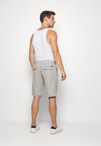 Men's light gray shorts made of linen blend, featuring back pockets, a relaxed fit, and paired with a white tank top and white sneakers.