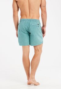 Turkio spalvos maudymosi šortai, pagaminti iš lengvos medžiagos, su elastinga juosta ir užtrauktuku užsegama užpakaline kišene. Textūruotas paviršius.