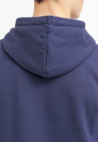 Felpa blu navy con un tessuto morbido e testurizzato. Presenta un cappuccio arrotondato e un design semplice, enfatizzando comfort e indossabilità.