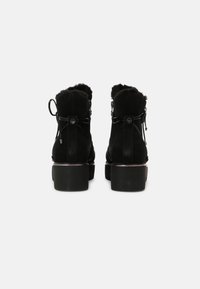 Bottines en suède noir avec doublure en shearling, à bout arrondi et talon épais. Présente des liens décoratifs à l'arrière pour un détail supplémentaire.