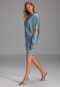 Haut en chiffon bleu clair avec des manches amples, associé à une jupe bleu clair froncée arrivant au genou. Modèle portant des talons argentés à lanières.